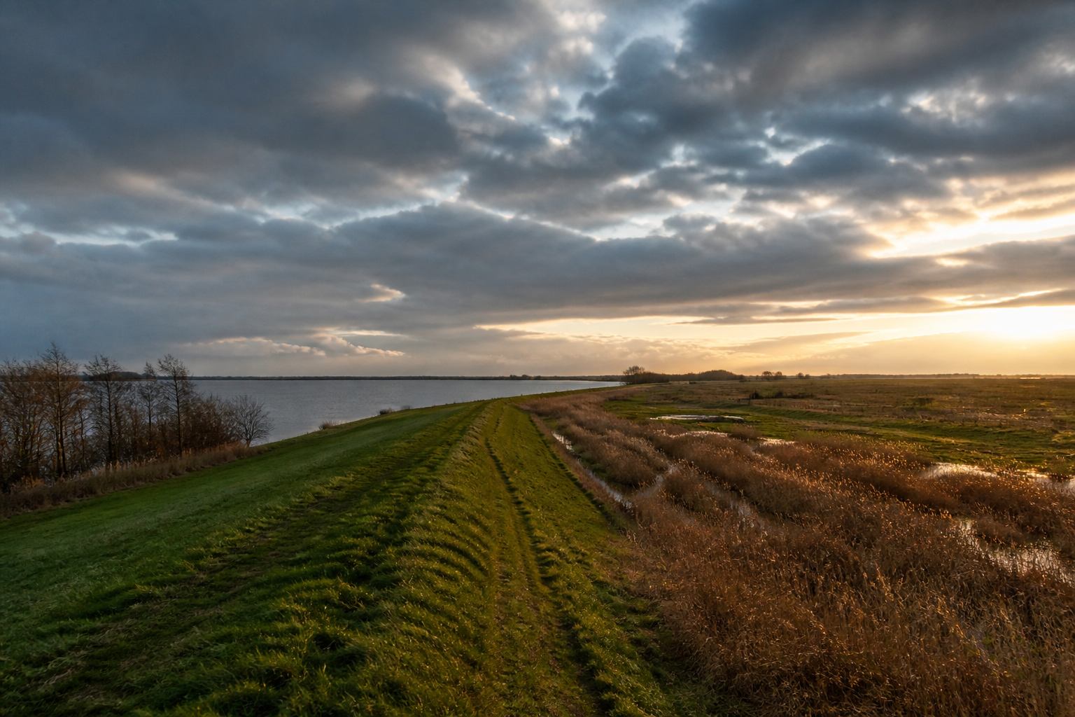 Wide northern German sky over lake, meadow and a thin dike line to the horizon